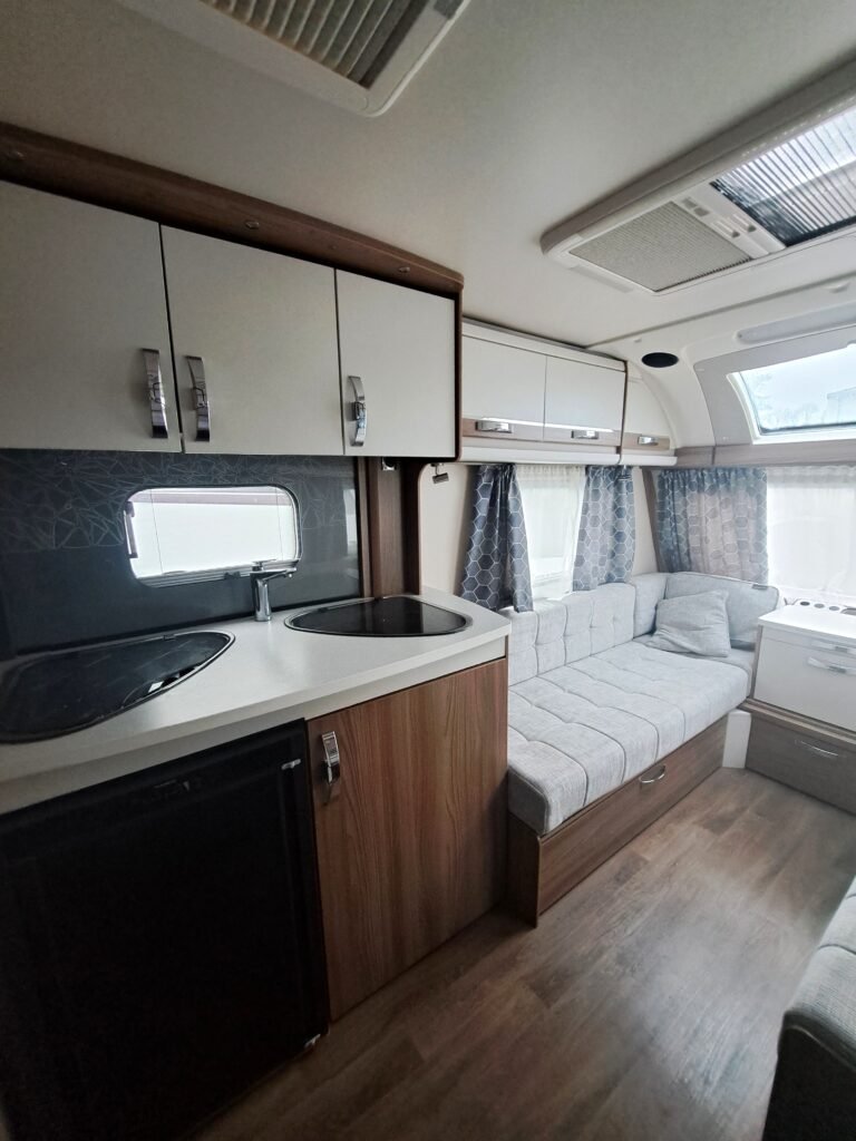 Interiér moderního karavanu s kuchyňkou, pohodlným sezením a úložným prostorem. Ideální pro cestování a rekreaci.