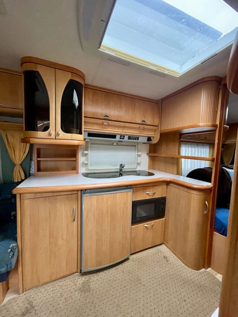 Kuchyňský prostor v karavanu se dřevěnými skříňkami a moderními spotřebiči. Ideální pro pohodové cestování!