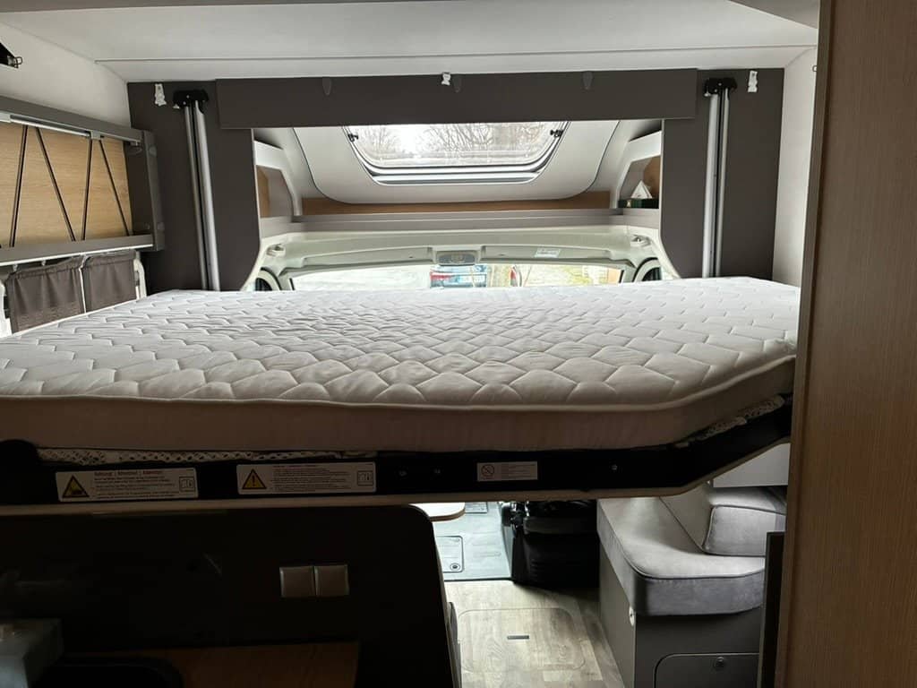 Obrázek ukazuje interiér obytného auta s rozkládací postelí. Komfortní a praktický design pro cestování.