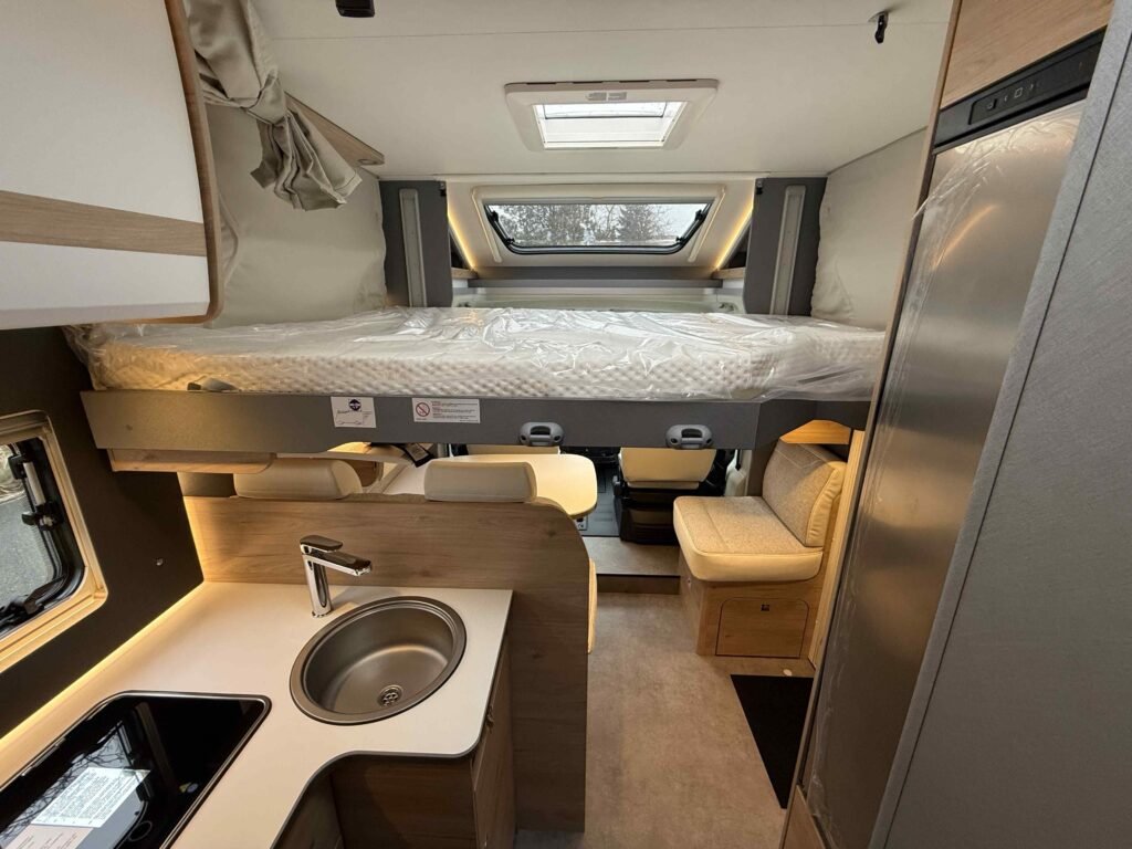 Moderní obytné auto s praktickým interiérem a lůžkem nad kuchyňskou linkou. Ideální pro pohodové cestování.