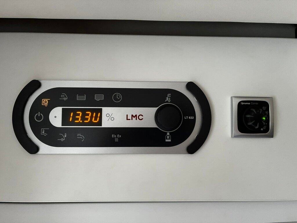 Obrázek ukazuje ovládací panel obytného auta značky LMC s informacemi o baterii a topení.