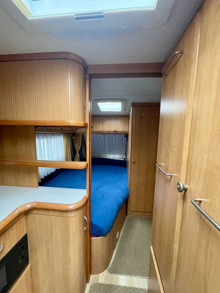Interiér karavanu s dřevěnými prvky a modrou postelí, ideální pro pohodlné cestování.