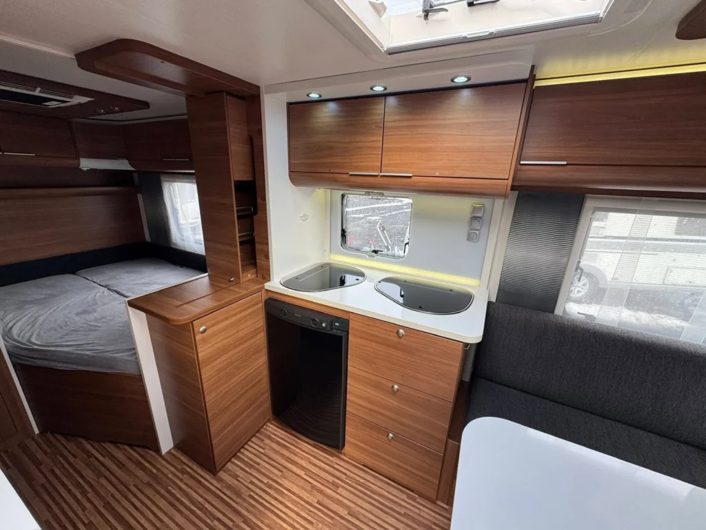 Moderní karavan s praktickou kuchyní a ložnicí. Stylové dřevo a dostatek úložného prostoru. Ideální na cestování.