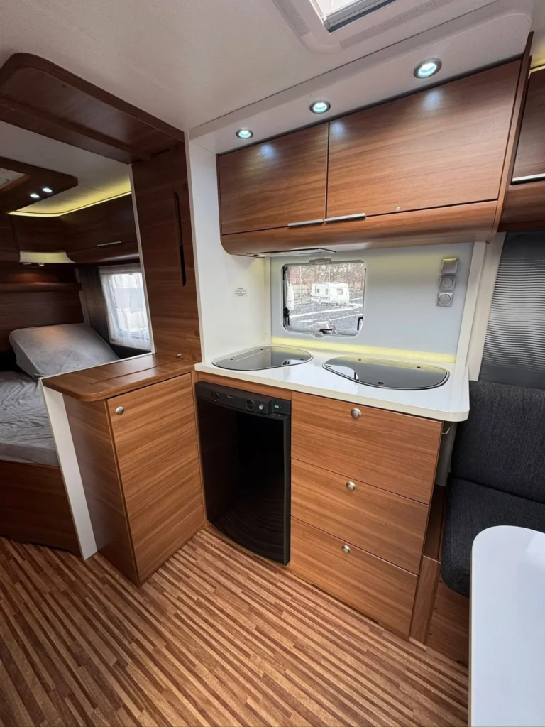 Moderní interiér karavanu s dřevěným nábytkem a kuchyňským koutem. Ideální pro pohodlné cestování.