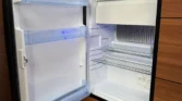 Obrázek ukazuje lednici značky Dometic uvnitř obytného vozu, ideální pro kempování. Kvalitní zařízení pro uchování potravin.