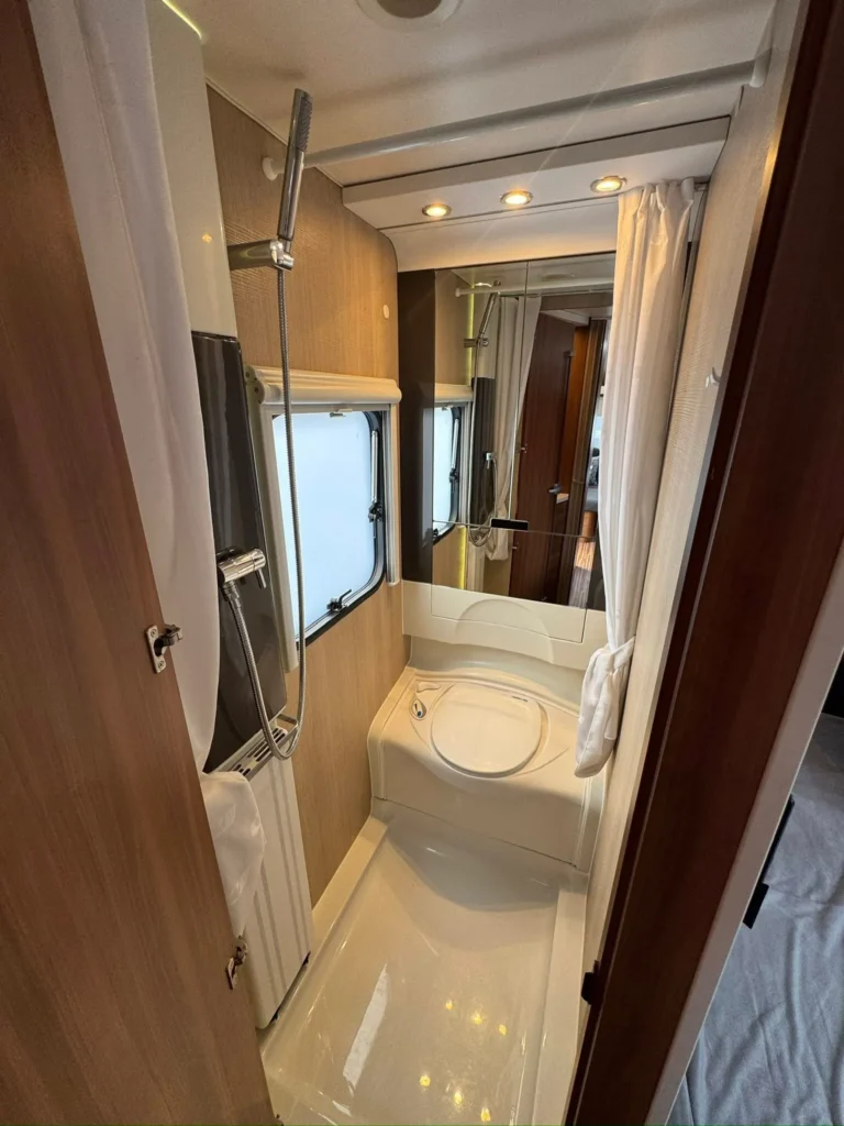 Obrázek zobrazuje moderní koupelnu v obytném autě, vybavenou sprchou a toaletou. Interiér je elegantní a praktický.