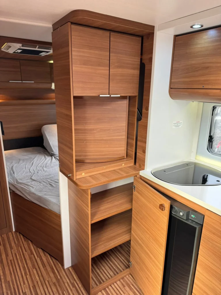 Interiér moderního karavanu, elegantní dřevěné skříně a kuchyňka pro pohodlné cestování.