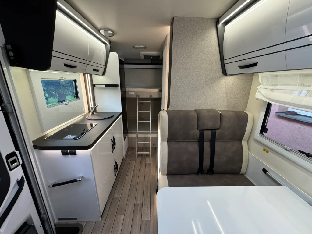 Obrázek interiéru moderního obytného auta s kuchyní a pohodlným sezením.