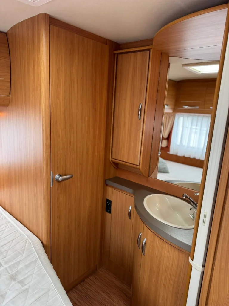 Obrázek interiéru karavanu s dřevěnou úpravou a koupelnovým koutem. Ideální pro kempování a cestování.