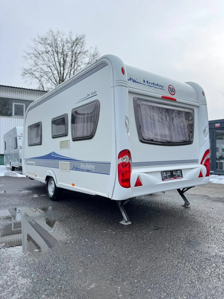 Karavan Mein Hobby De Luxe zaparkovaný na asfaltu, ideální pro pohodlné cestování a dobrodružství.