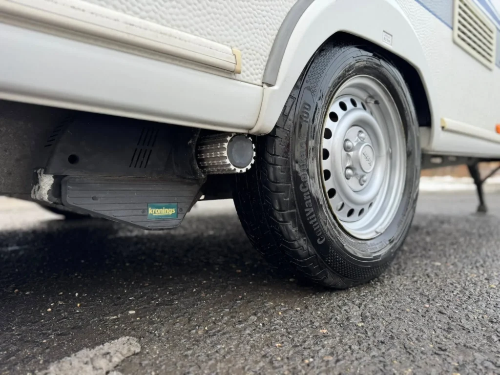 Obrázek zobrazuje karavan s označením kronings. Detailní pohled na kolo a podvozek.
