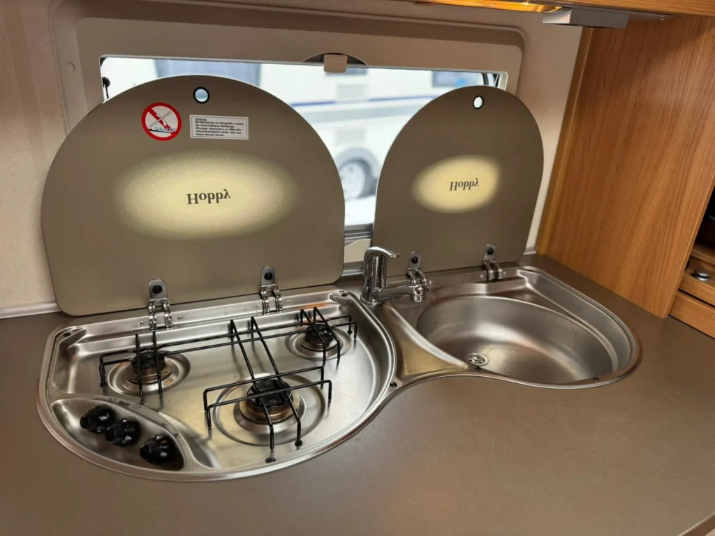 Obrázek ukazuje kuchyňku obytného auta s dřezem a vařičem značky Hoppla. Ideální pro přípravu jídel na cestách.
