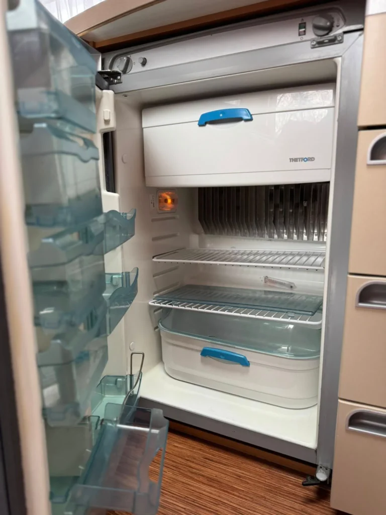 Obrázek ukazuje lednici značky Thetford ve vybavení obytného vozu. Ideální pro cestování s komfortem.