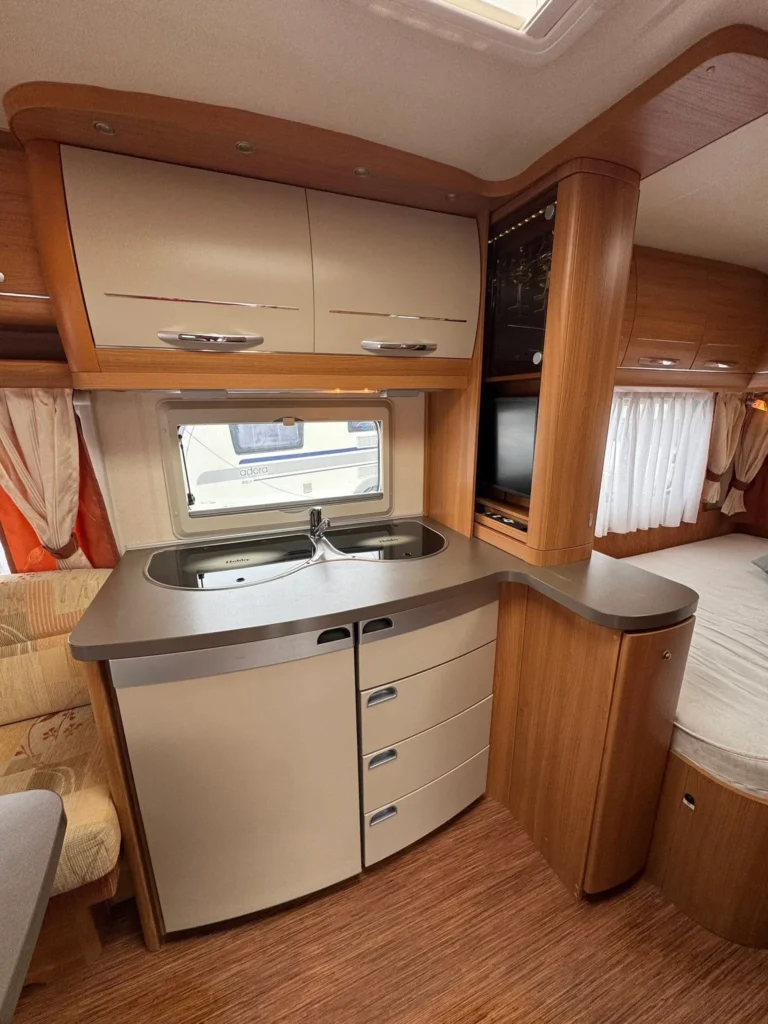 Obrázek interiéru karavanu s moderním kuchyňským koutem a úložnými prostory. Elegantní, praktické řešení pro cestování.