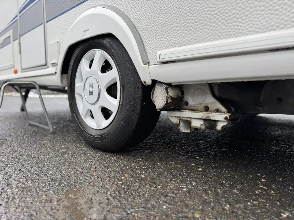 Na obrázku je obytný přívěs s viditelným kolem a podvozkem, ukazující rostlou část. Značka a model nejsou znatelné.