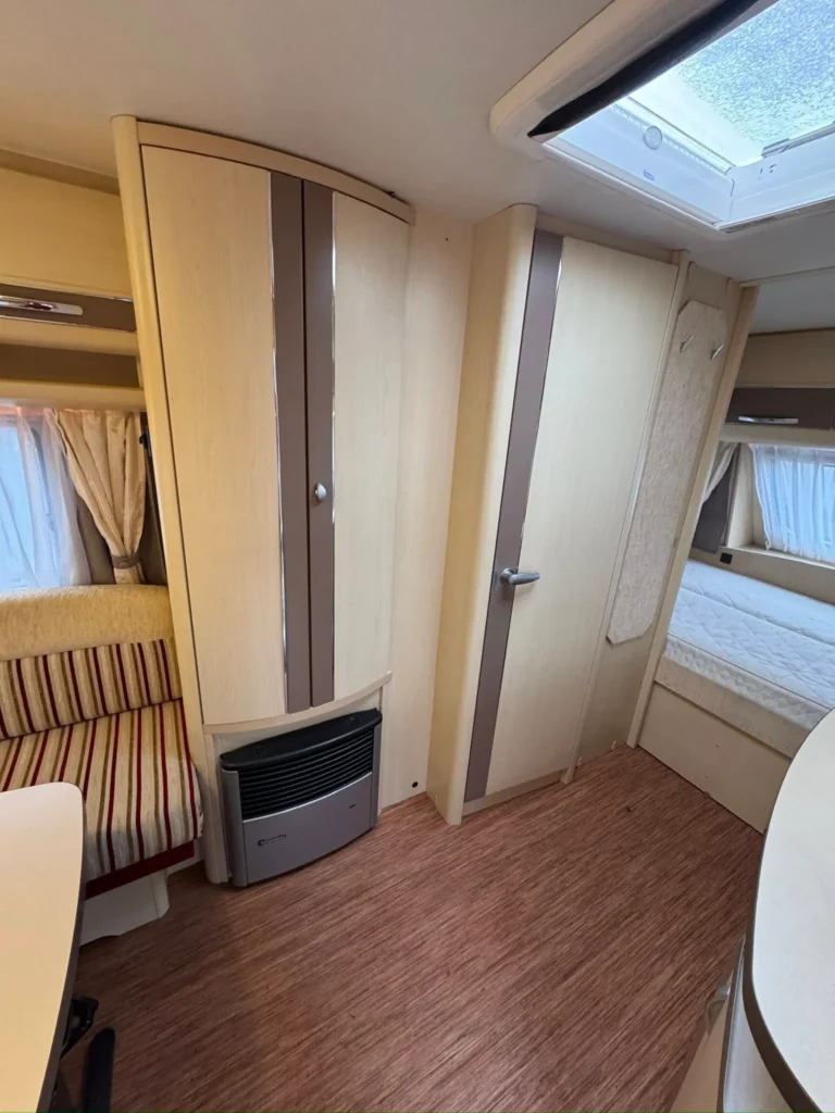 Interiér obytného přívěsu s dřevěnými obklady, sedačkou se striped potahem, skříní a topením.