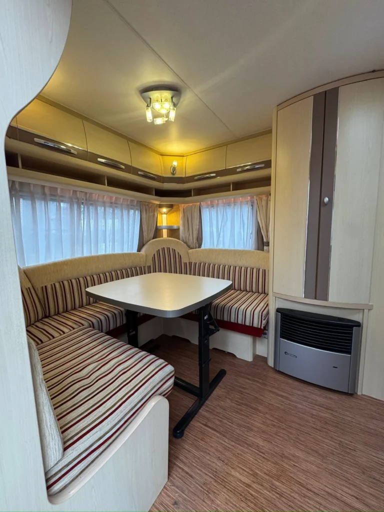 Interiér obytného přívěsu se sedačkami se vzorem a stolkem. Příjemné osvětlení a praktické úložné prostory.