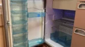 Na obrázku je interiér karavanu s lednicí Dometic, viditelné modré zásobníky a police.