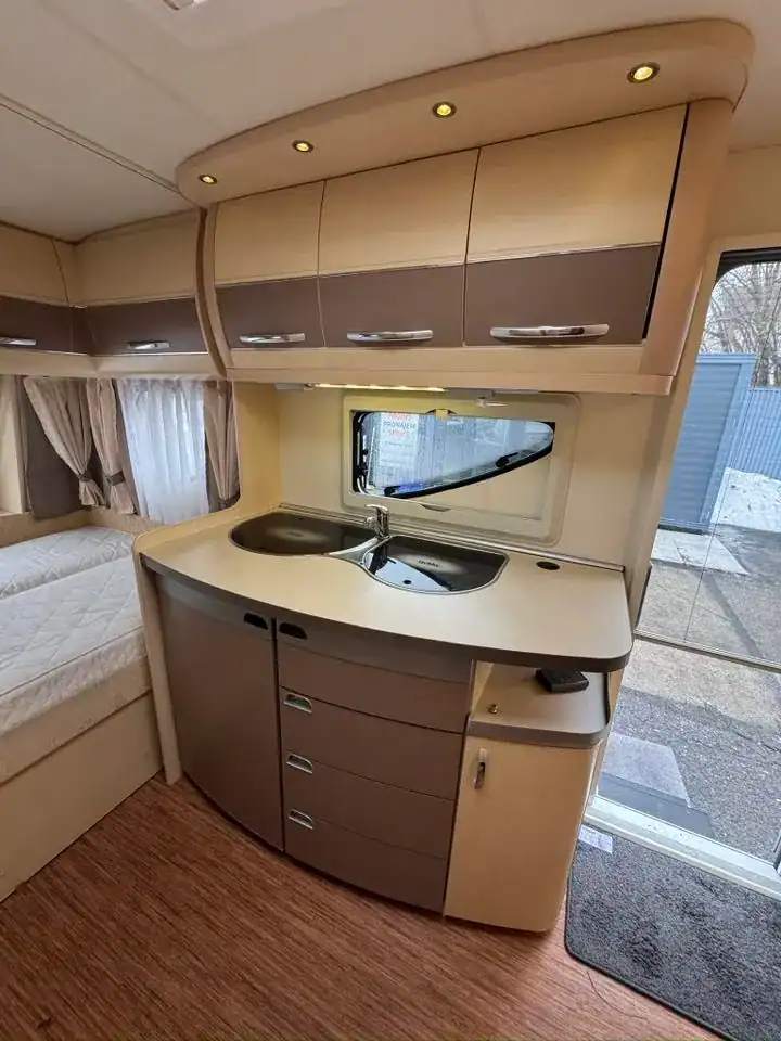 Interiér obytného přívěsu s kuchyňským koutem, dřezem a úložnými prostory v moderním designu.