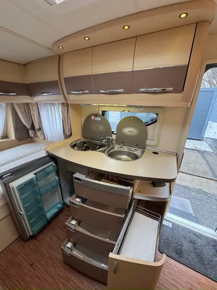 Interiér karavanu s kuchyňským koutem, dřezem a chladničkou. Moderní design, funkční uspořádání, světlé barvy.