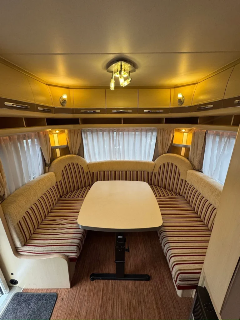 Interiér karavanu s pohodlnými sedačkami a stolkem. Světlé barvy a decentní osvětlení.