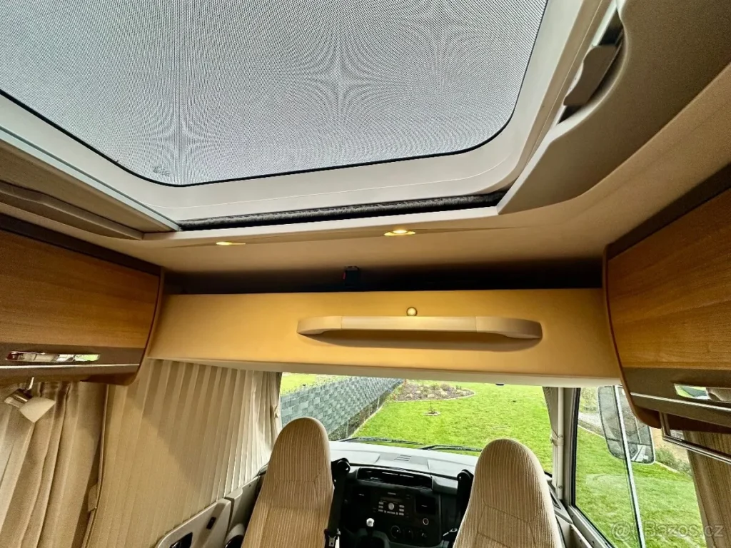 Interiér obytného auta s moderním designem, stropním oknem a pohodlnými sedačkami. Ideální pro cestování.