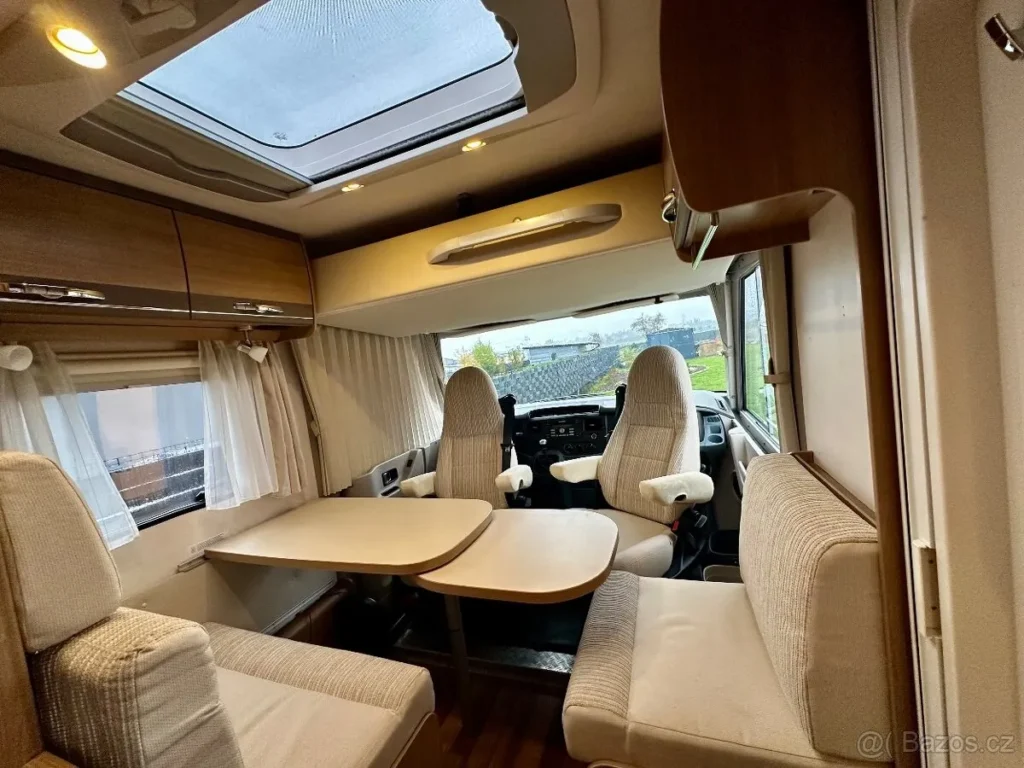 Interiér obytného auta s prostorným sezením a kuchyňským koutem. Příjemné a světlé prostředí vhodné na dovolenou.