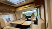 Interiér obytného auta s prostorným sezením a kuchyňským koutem. Příjemné a světlé prostředí vhodné na dovolenou.