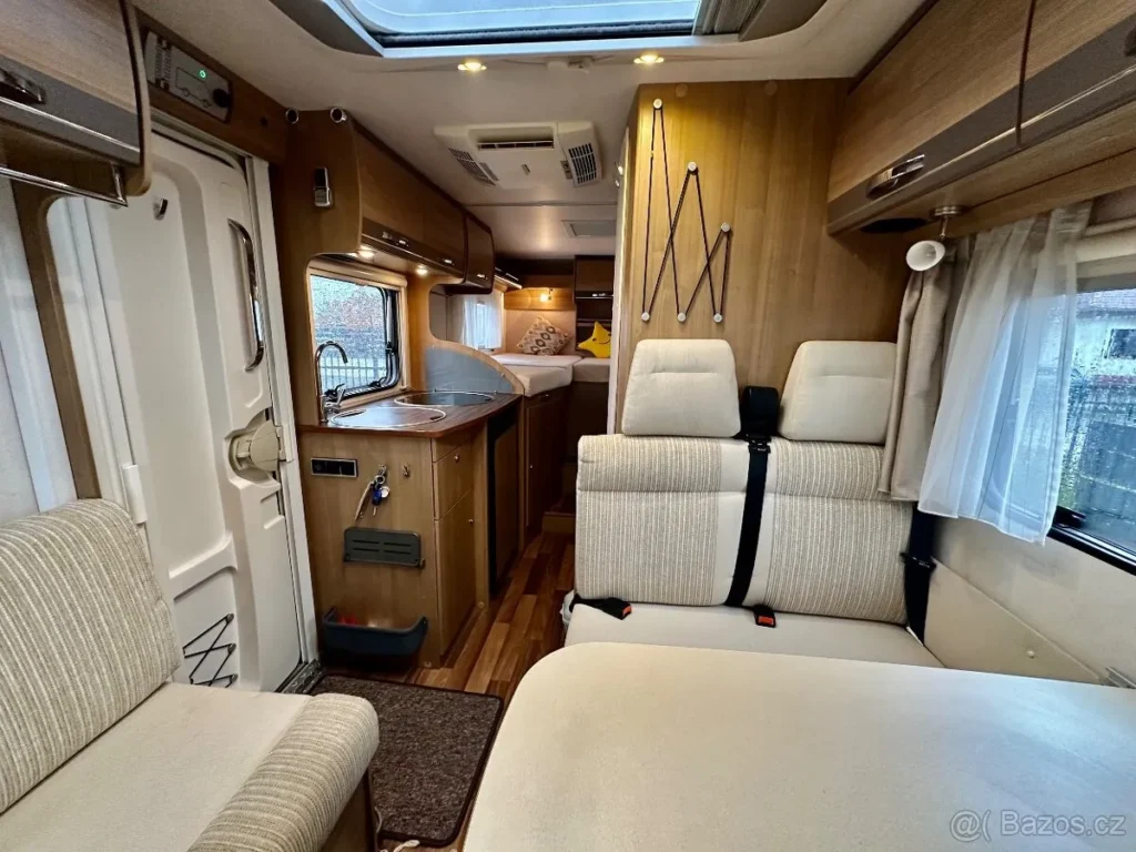 Obrázek interiéru obytného auta, pohodlné posezení a kuchyňka, ideální pro cestování a kempování.