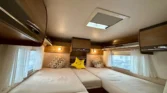 Pohodlný interiér karavanu s útulnými postelemi a úložným prostorem. Ideální pro odpočinek na cestách.