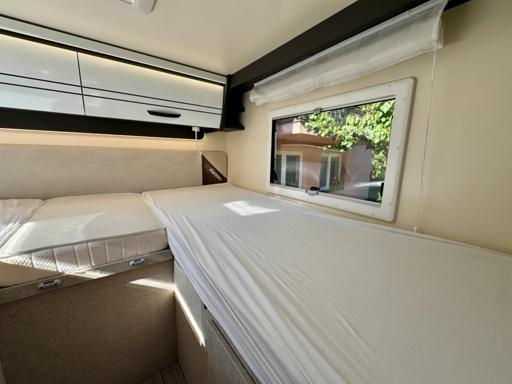 Obrázek interiéru karavanu s pohodlnými lůžky a oknem pro přirozené osvětlení.