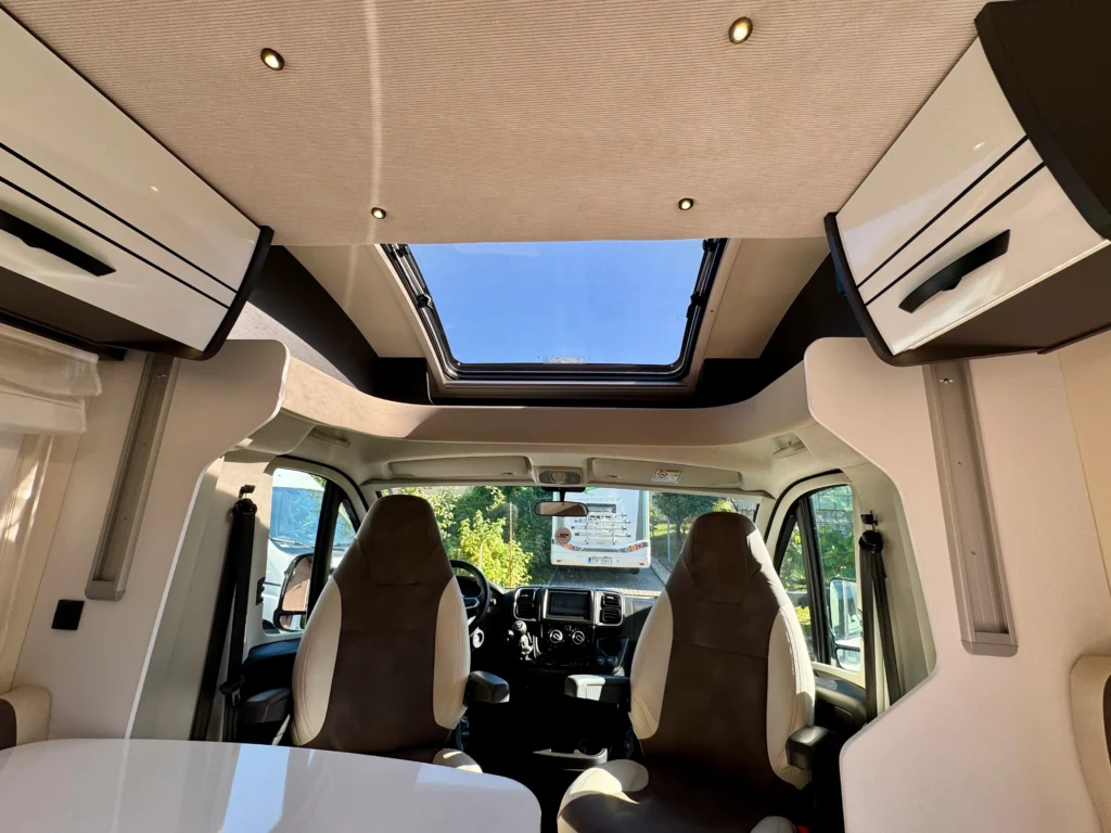 Interiér obytného auta s moderním designem, prosklenou střechou a komfortními sedadly. Ideální pro cestování.