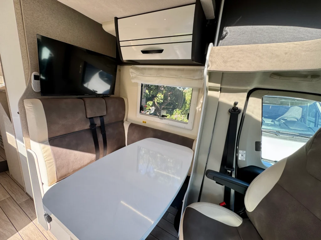 Interiér obytného auta s jídelním stolem a televizorem. Komfortní zařízení pro cestování.