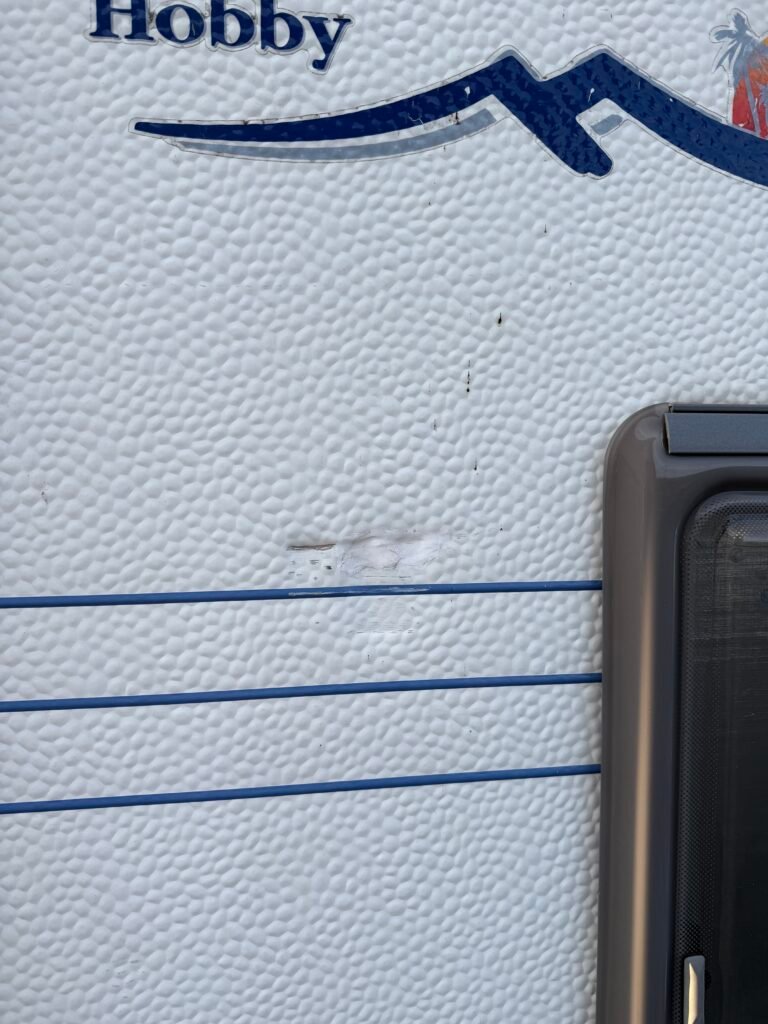 Na obrázku je karavan značky Hobby se drobnými oděrkami na povrchu. Ideální pro cestování a dovolenou.