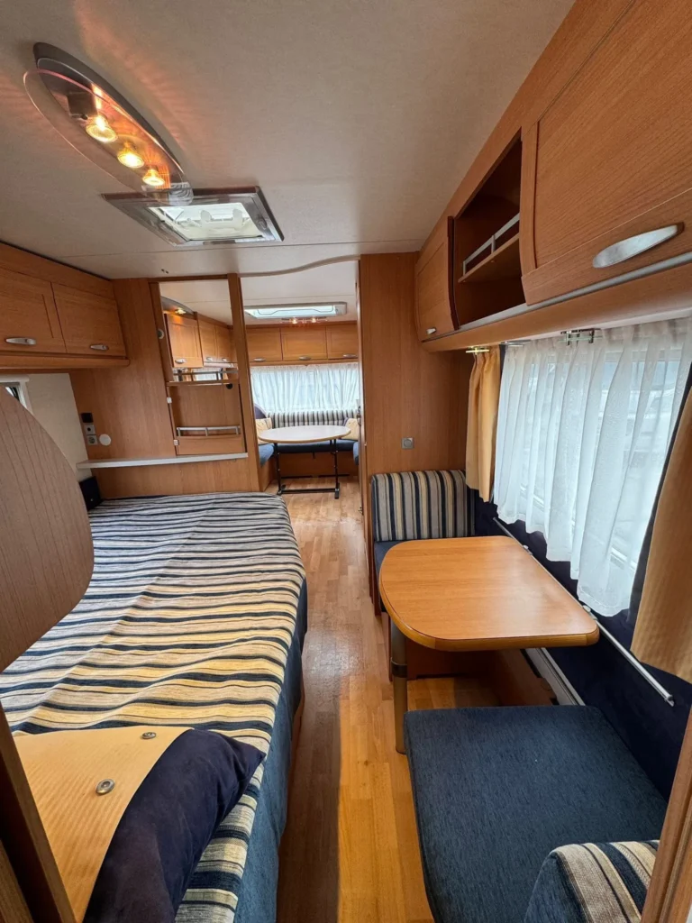 Obrázek interiéru karavanu s prostornou ložnicí a útulným posezením. Ideální pro cestování s rodinou.