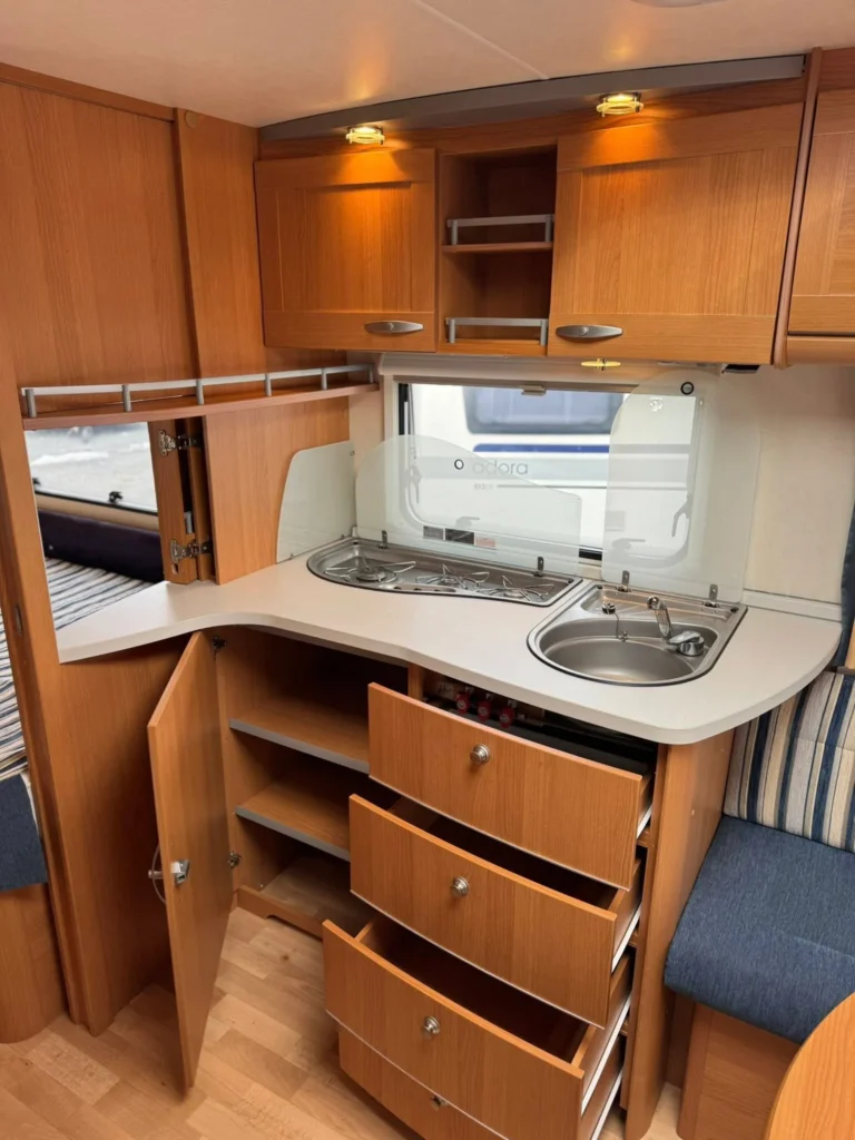 Interiér karavanu s kuchyňským koutem a úložnými prostory. Moderní a prostorný design pro pohodlné cestování.