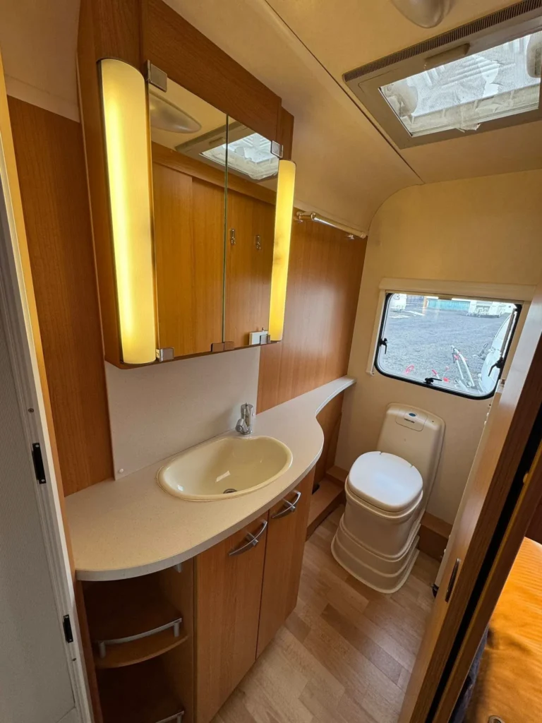 Interiér moderního karavanu s koupelnou a toaletou, příjemné dřevo a osvětlení pro pohodlí.