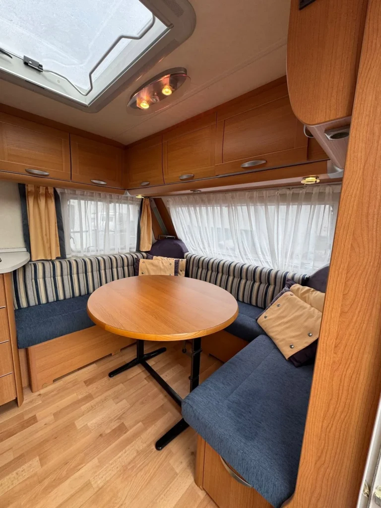 Útulný interiér karavanu s jídelním stolem a pohodlnými sedacími místy. Ideální pro relaxaci na cestách.