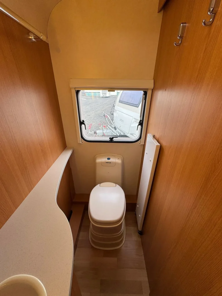 Obrázek interiéru karavanu s toaletou a dřevěným obložením. Příjemný a praktický prostor pro cestování.