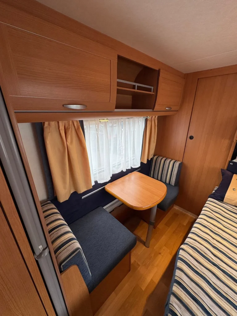 Obrázek interiéru karavanu s dřevěnými prvky, pohodlným sezením a stolem pro relaxaci. Ideální pro cestování.
