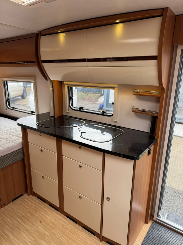 Interiér karavanu s praktickým kuchyňským koutem a úložným prostorem. Elegantní design a moderní vybavení.
