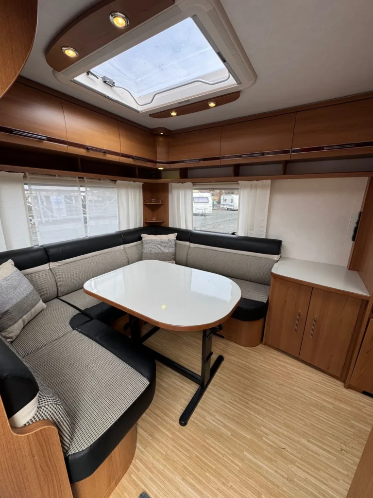 Obrázek interiéru karavanu s pohodlným sezením a stolem, ideální pro relaxaci a posezení.