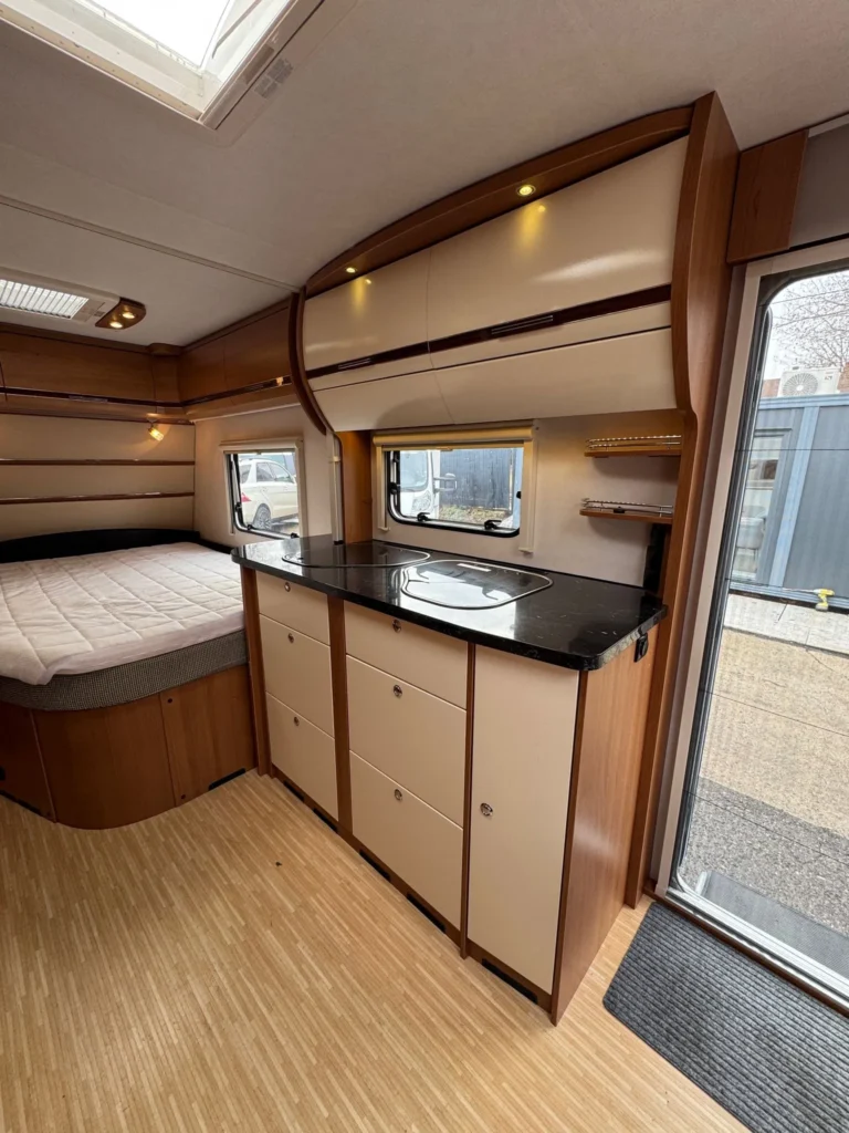 Obrázek interiéru moderního karavanu s kuchyňkou a ložnicí. Elegantní dřevěné prvky a prostor pro pohodlí.