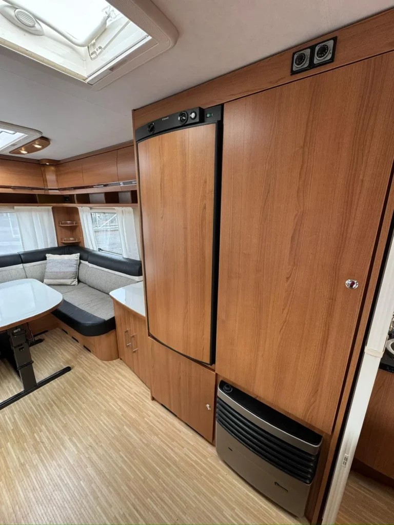 Interiér karavanu s dřevěnými prvky a sezení pro pohodlné posezení. Vybavení zahrnuje lednici a klimatizaci.