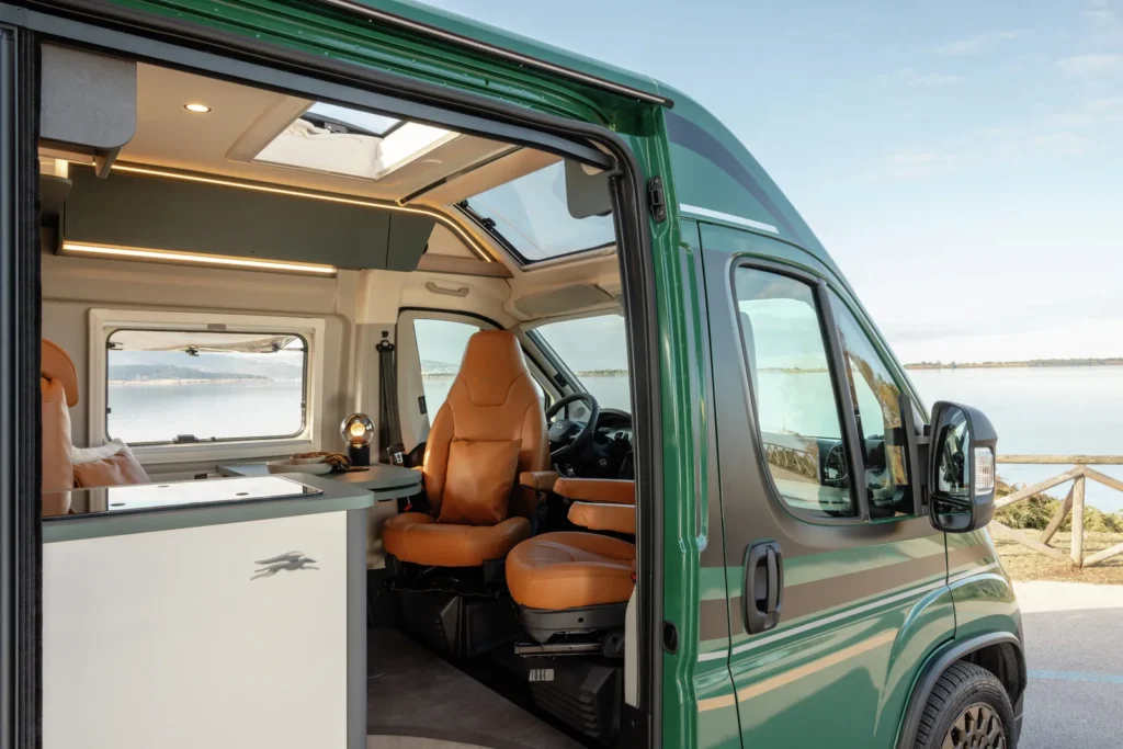 Obytné auto s moderním interiérem a velkým oknem, ideální pro cestování a odpočinek u vody.