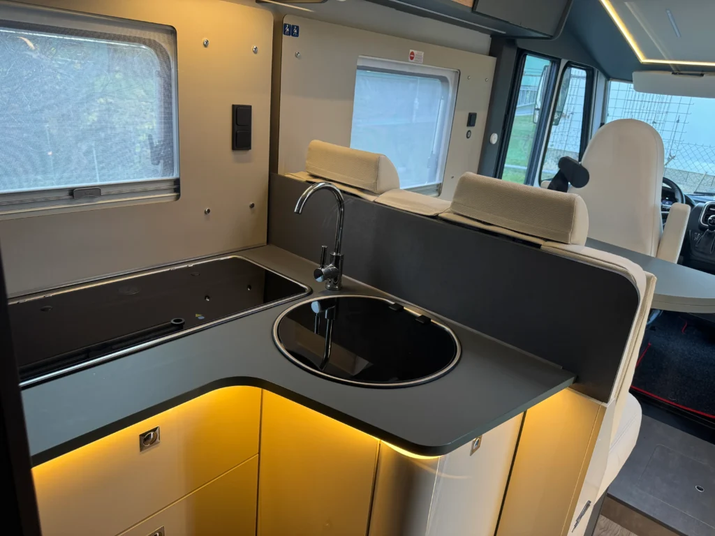 Obrázek zobrazuje moderní obytné auto s elegantní kuchyňskou linkou a funkcionalitou.