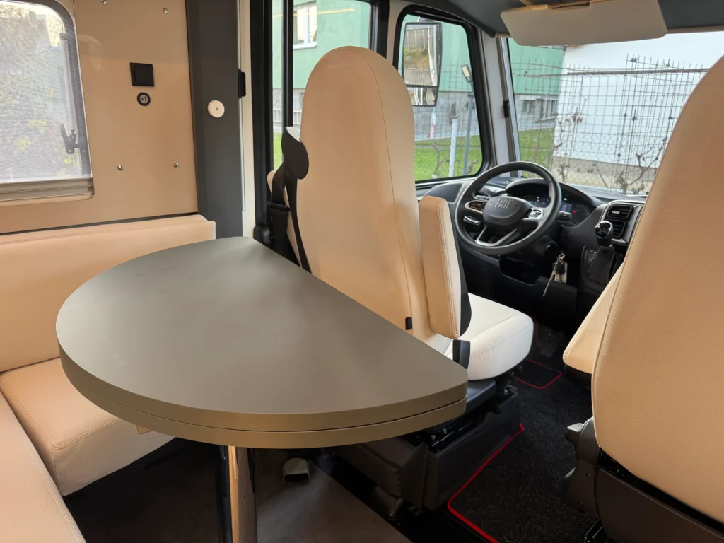 Obrázek interiéru obytného auta Fiat, stylové a prostorné místo s moderním stolem a pohodlnými sedadly.