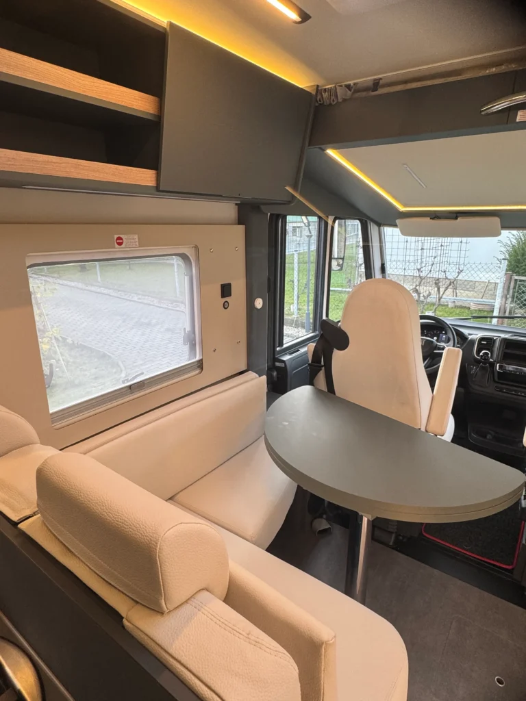 Obytné auto s moderním interiérem, bílými sedačkami a kulatým stolem, ideální pro cestování.