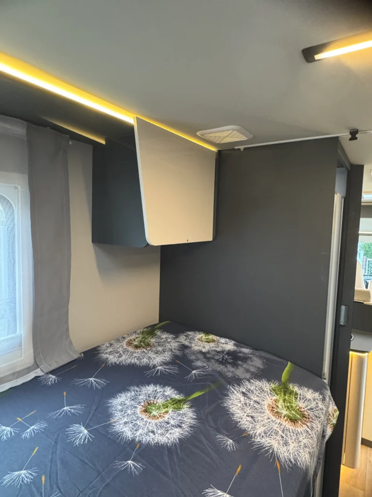 Obrázek interiéru moderního obytného vozu, útulně zařízený s postelí a designovým osvětlením.