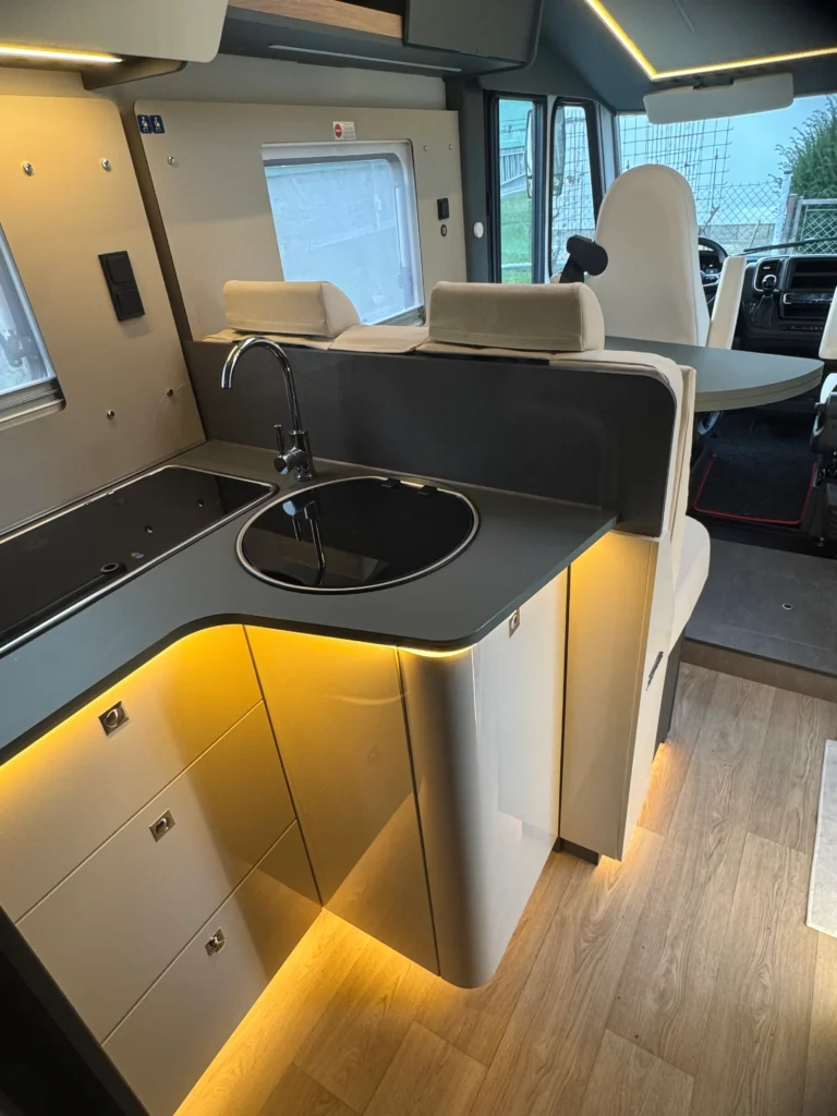 Interiér obytného auta s moderním kuchyňským koutem a osvětlovacími prvky. Komfortní a praktický prostor.